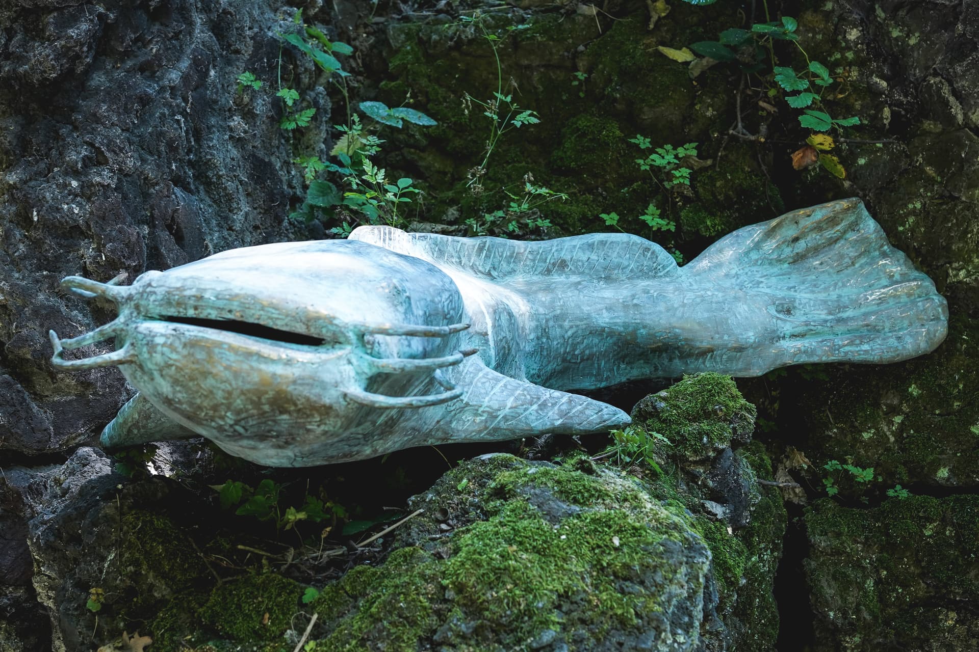 A blue stone sculpture of a fish sits on top of a moss covered rock.