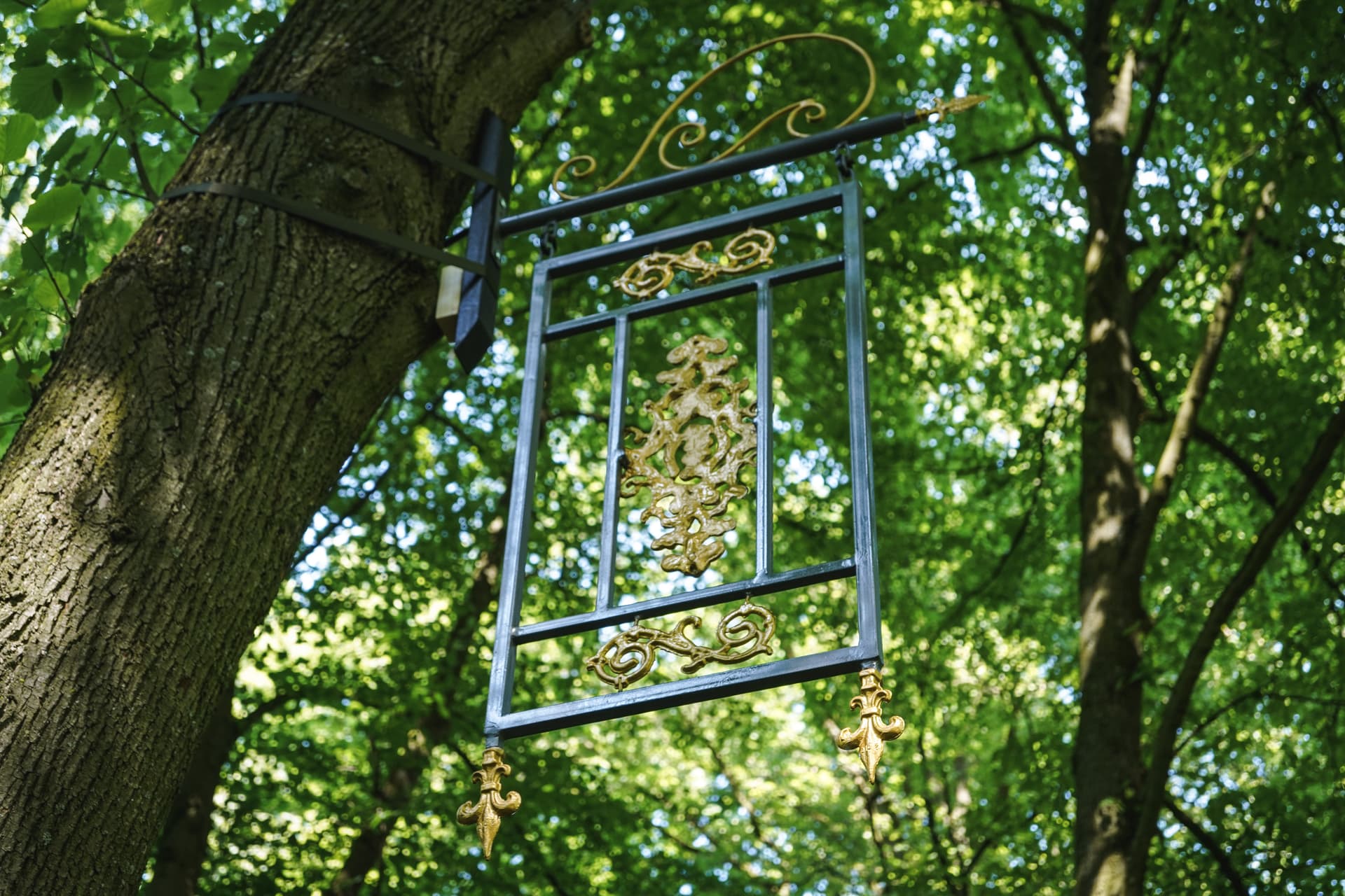 A metal sculpture hangs from the branches of a tree in the park.